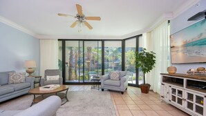 Una sala de estar con sofá, sillón, mesa de centro, mueble para televisión y ventilador de techo.