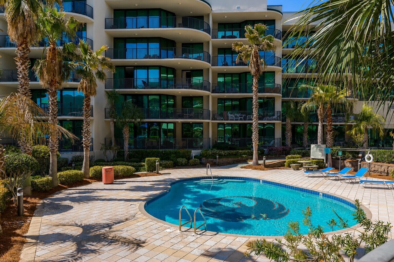 Un hôtel doté d’une piscine, de palmiers et d’un immeuble à plusieurs étages avec des balcons.
