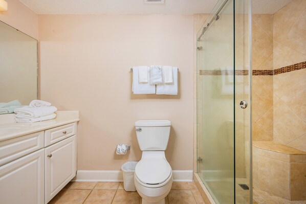 A bathroom with a toilet, a glass shower enclosure, a sink with a mirror, and a towel rack with folded towels.