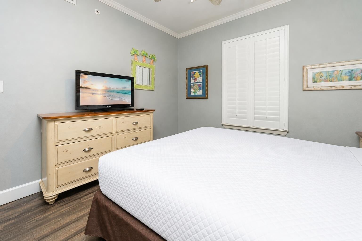 Un dormitorio con cama, cómoda, televisor y decoración en la pared.