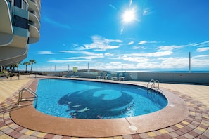 A swimming pool with a sunlit sky, a brick deck, and a view of the ocean. - ~Beach Front~ 2 Bedroom @ Phoenix IX (Orange Beach)