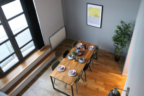 A dining area with a wooden table set for four, chairs, a radiator, a framed picture on the wall, and a potted plant. - 4B Loft Penthouse Industrial City views (Coventry)