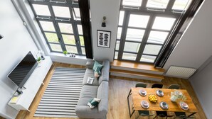 Un salon moderne avec un canapé gris, une table à manger dressée pour quatre personnes et de grandes fenêtres donnant sur l’extérieur.