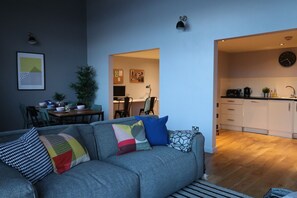 A modern living room with a grey sofa, colorful cushions, and a dining area in the background. - 4B Loft Penthouse Industrial City views (Coventry)
