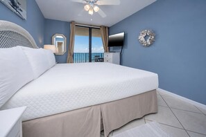 A bedroom with a large bed, a ceiling fan, a TV, and a balcony with curtains. - Phoenix II 2082 - Beachfront Gulf Views (Orange Beach)