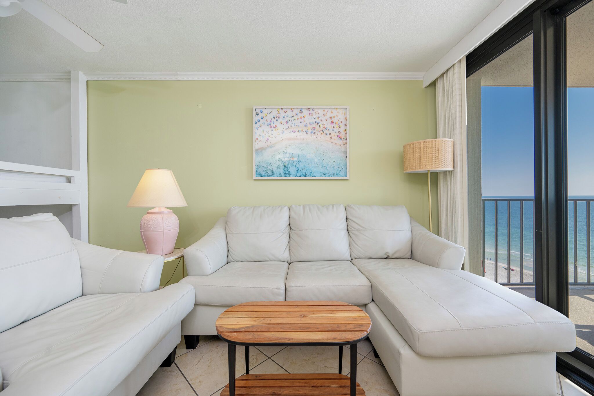 A modern living room with a white sofa, a wooden coffee table, a pink lamp, and a painting on the wall.