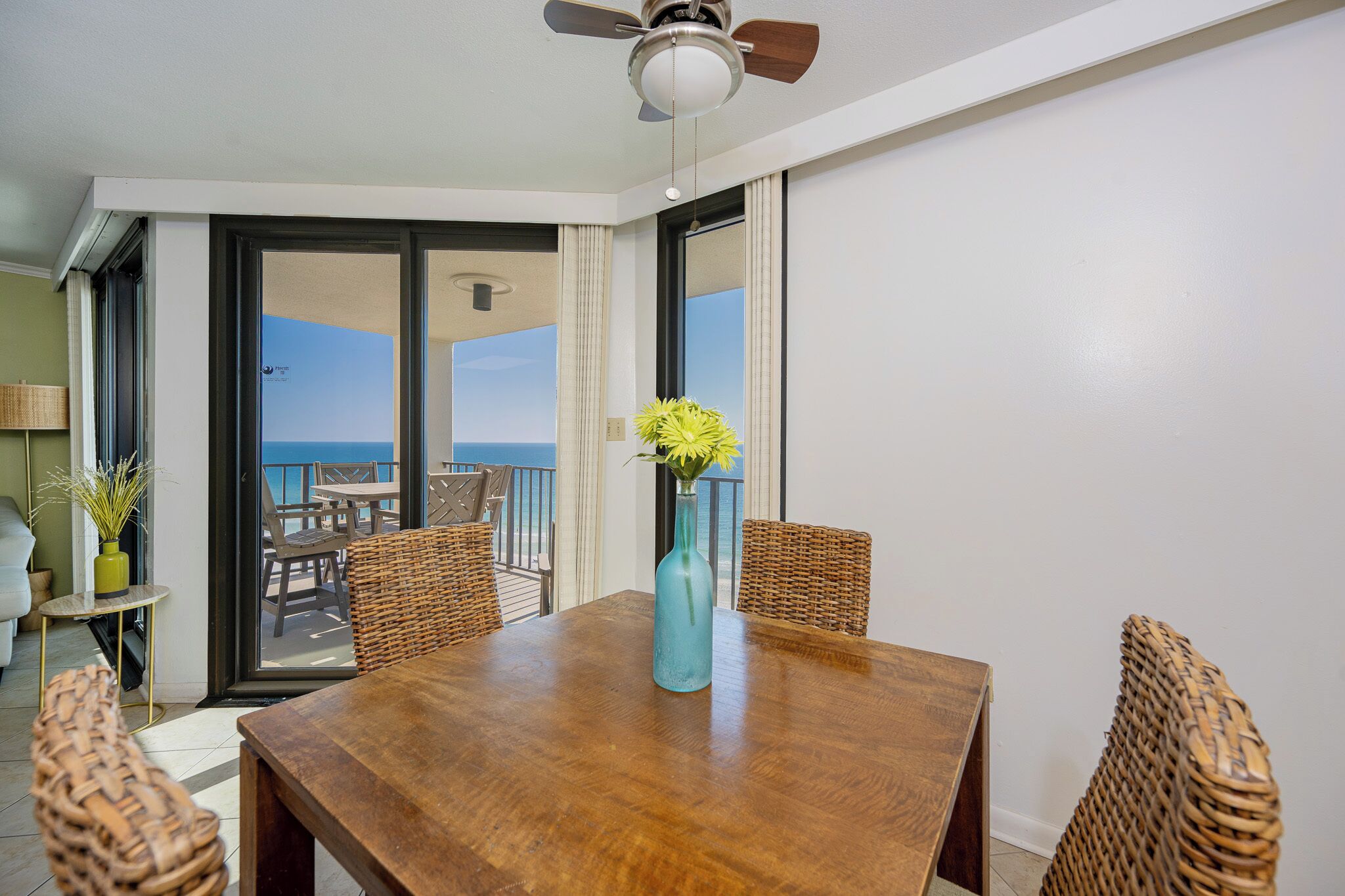 A dining area with a wooden table, wicker chairs, and a vase with flowers.