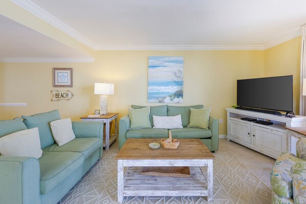 A living room with two green sofas, a coffee table, a TV, and a painting on the wall.