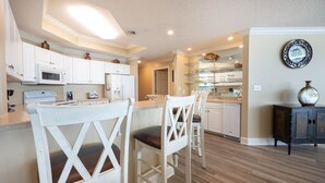 A modern kitchen with white cabinetry, a microwave, and a dining area with white chairs. - Phoenix West - 3 Bedroom (Orange Beach)