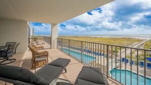 A balcony with lounge chairs, a pool, and a view of the beach and ocean.