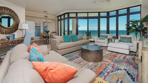 A spacious living room with a large window overlooking the ocean, a round coffee table, and a variety of seating options. - The Oasis at Orange Beach, formerly known as Phoenix West II, Unit 404 (Orange Beach)