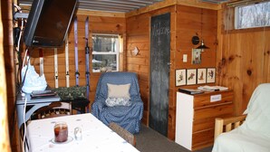 Interior acogedor de una cabaña con paredes de madera, una mesa con una vela, una silla con cojín y una pizarra con un mensaje de bienvenida.