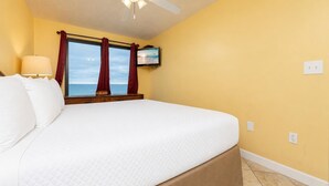 A hotel room with a large bed, a TV mounted on the wall, and a view of the sea through the window. - GULF FRONT! Two Bedroom at Island Winds (Gulf Shores)