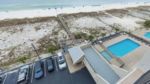 A beachside hotel with a swimming pool, a parking area, and a view of the beach.