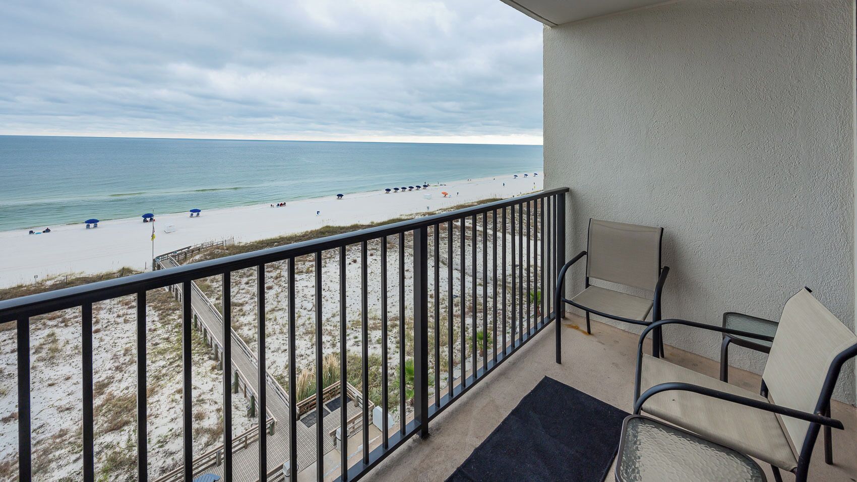 A balcony with a view of a beach, a chair, and a small rug.