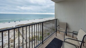 A balcony with a view of a beach, a chair, and a small rug. - GULF FRONT! Two Bedroom at Island Winds (Gulf Shores)