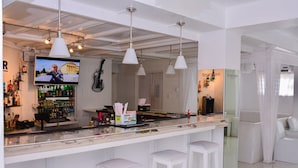 Eine Bar mit weißen Barhocker, einem an der Wand montierten Fernseher und verschiedenen Flaschen und Gläsern auf der Theke.