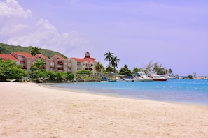 A beachfront hotel with multiple buildings, a sandy beach, and boats in the water.