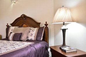 A neatly made bed with a floral bedspread and multiple pillows, a classic wooden headboard, and a bedside table with a lamp and a book.