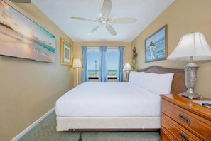 Une chambre d’hôtel avec un lit, un ventilateur de plafond, une table de chevet avec une lampe, une commode et un tableau au mur.