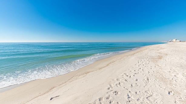 A beach with a clear sky, calm sea, and footprints in the sand.