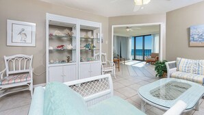A spacious living area with a balcony, wicker furniture, and a glass cabinet with decorative items. - **WEEKLY SPECIALS!** Phoenix III - Low Floor - 2 Bedroom (Orange Beach)