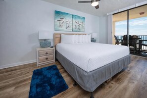 A bedroom with a bed, nightstand, lamp, artwork, and a view of the outdoors. - Reserved Parking with this Two Bedroom at Phoenix 5 (Orange Beach)