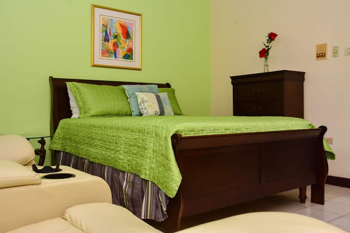 A bedroom with a green bedspread, a wooden headboard, and a nightstand with a vase of red flowers.