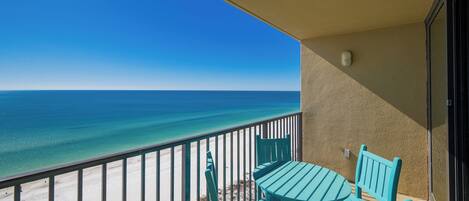 A balcony with a table and chairs, overlooking a beach and the ocean.