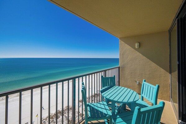 A balcony with a table and chairs, overlooking a beach and the ocean.