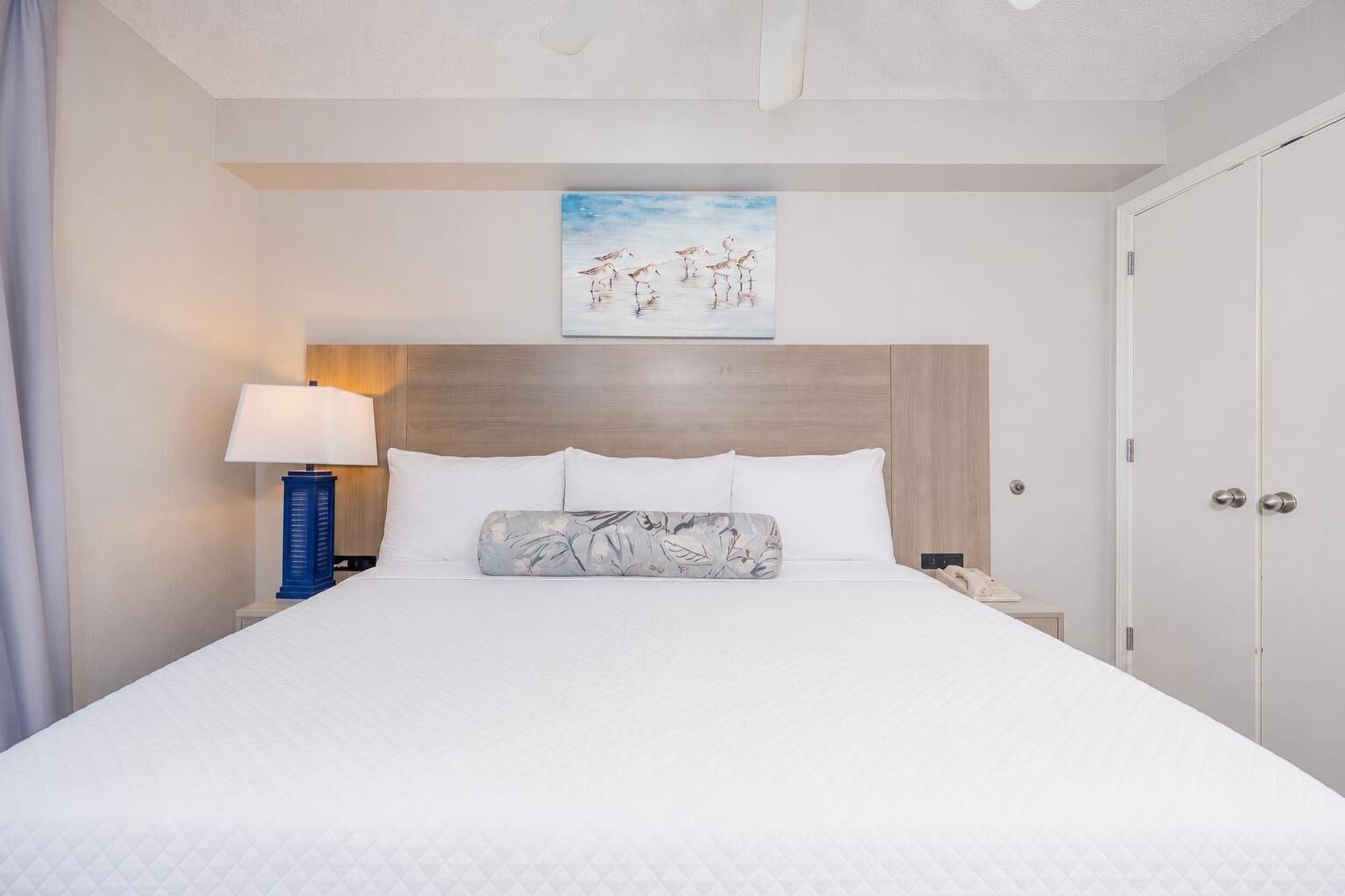 Een hotelkamer met een bed, nachtkastje, lamp, schilderij en een deur.