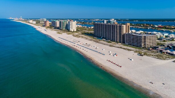 Un paisaje urbano costero con una larga playa de arena, edificios altos y un cielo azul despejado.