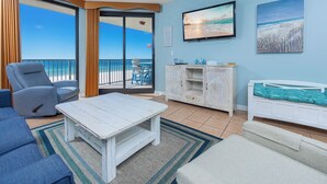 Una habitación con vistas al océano, una mesa de centro blanca, un sillón azul, un armario blanco y un televisor en la pared.