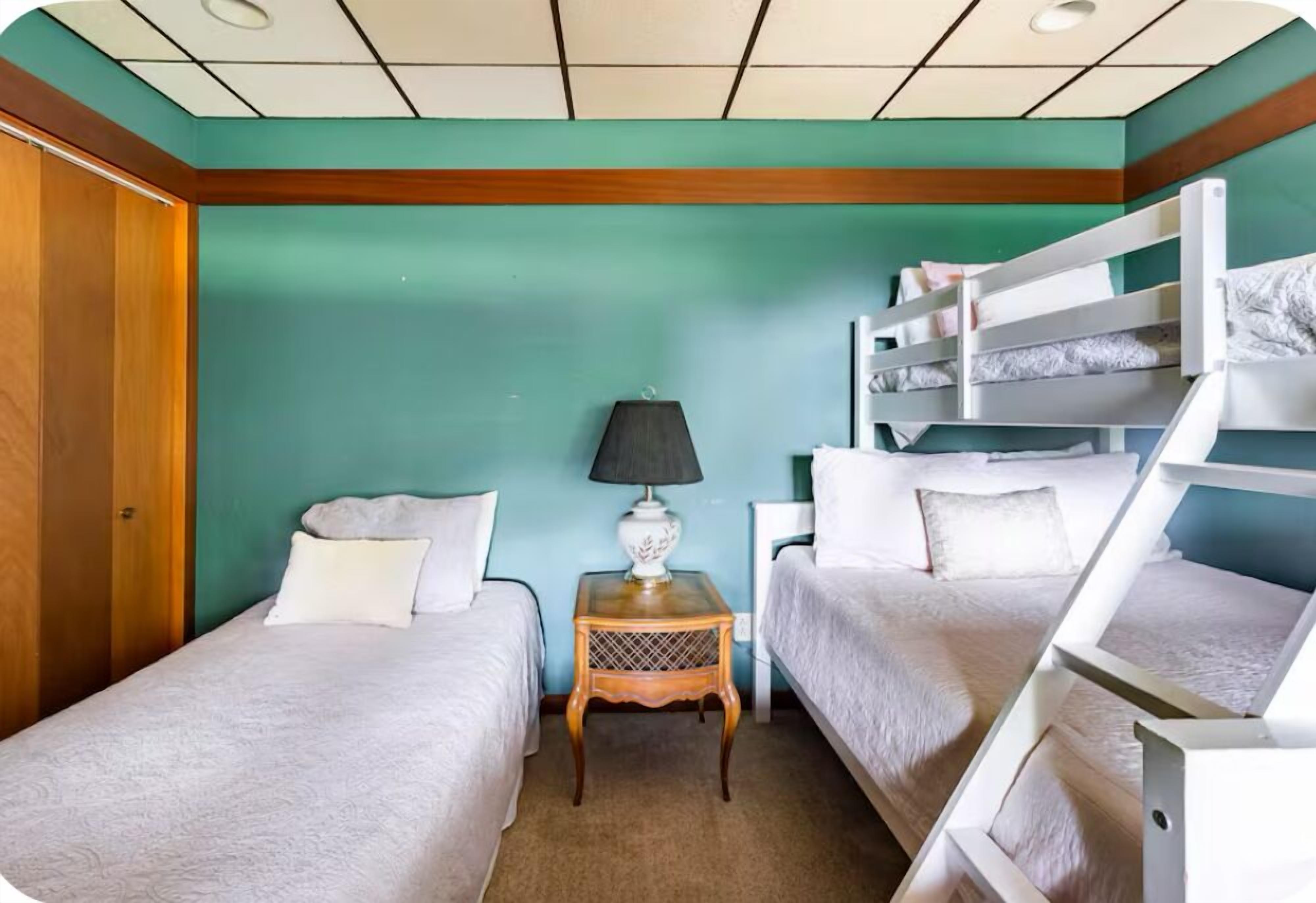 A room with two single beds, a small table with a lamp, and a bunk bed.
