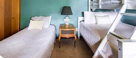 A room with two single beds, a small table with a lamp, and a bunk bed.