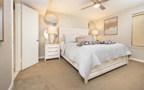 Une chambre à coucher avec un lit, des tables de chevet, un ventilateur de plafond et une fenêtre avec des stores.