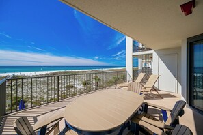 Un balcón con vista a la playa, una mesa, sillas y una barandilla.