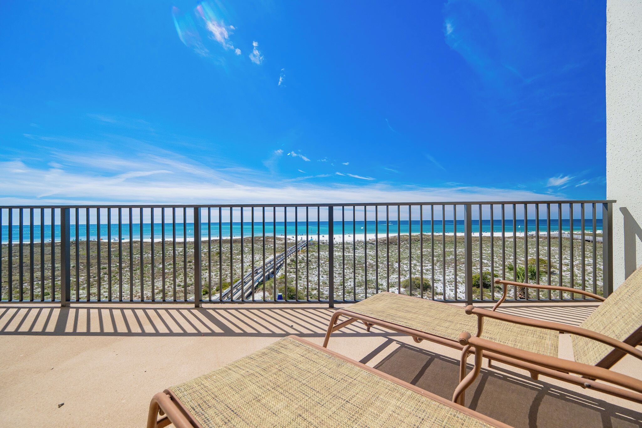 A balcony with a view of the beach and ocean, equipped with wicker lounge chairs.