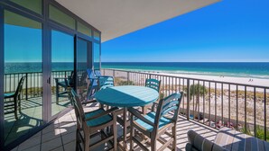 A balcony with a table and chairs, overlooking a beach with a clear view of the ocean. - The Oasis at Orange Beach, formerly known as Phoenix West II, Unit 302 (Orange Beach)