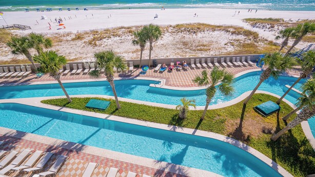 A pool area with multiple swimming lanes, lounge chairs, and palm trees. - The Oasis at Orange Beach, formerly known as Phoenix West II, Unit 302 (Orange Beach)