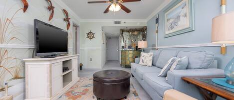 A living room with a television, a ceiling fan, a sofa, a coffee table, and a patterned rug.
