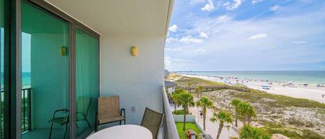 A balcony with a table and chairs, overlooking a beach with palm trees and a boardwalk.