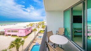 Uma varanda com vista para uma praia, uma piscina e um edifício cor-de-rosa.