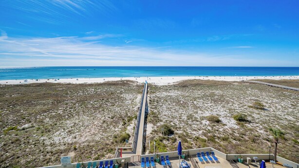 A beach view with a long pier, beach chairs, and a clear sky.