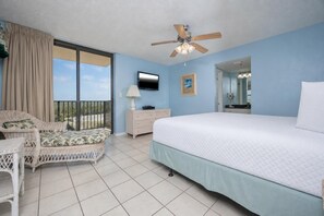 Un dormitorio con cama, televisor, ventilador de techo, ventana con cortinas y balcón.