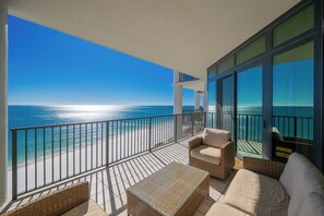 Uma varanda com vista para o oceano, móveis de vime e uma porta de vidro.