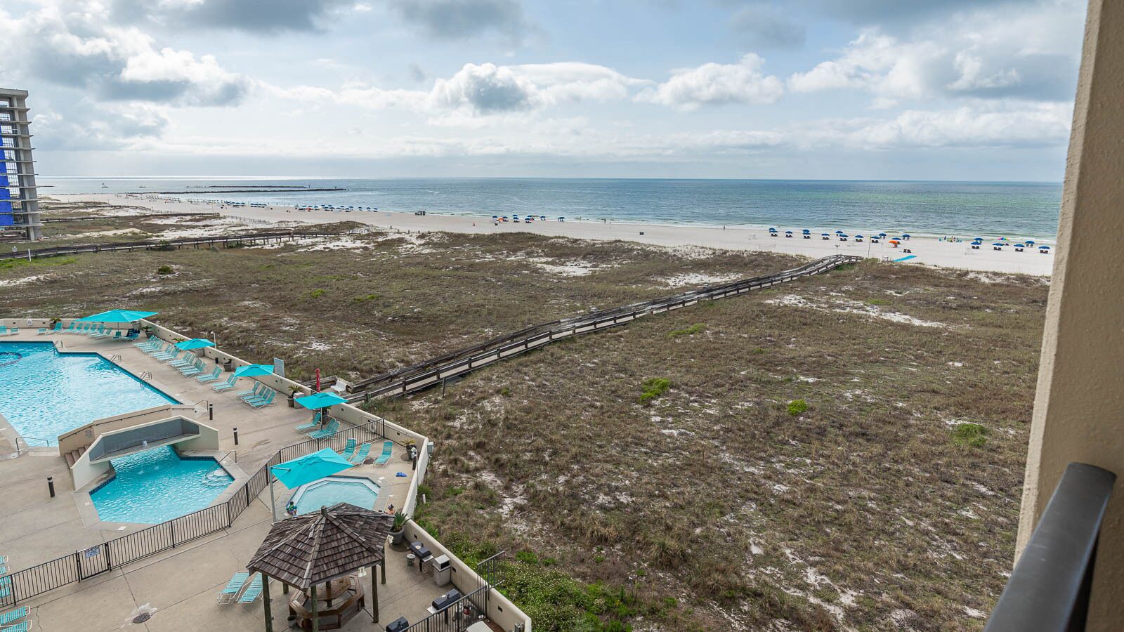 A beach view from a balcony overlooking a swimming pool with sun loungers and umbrellas.