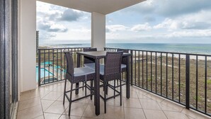 Un balcon avec une table et des chaises, donnant sur une plage et une piscine.