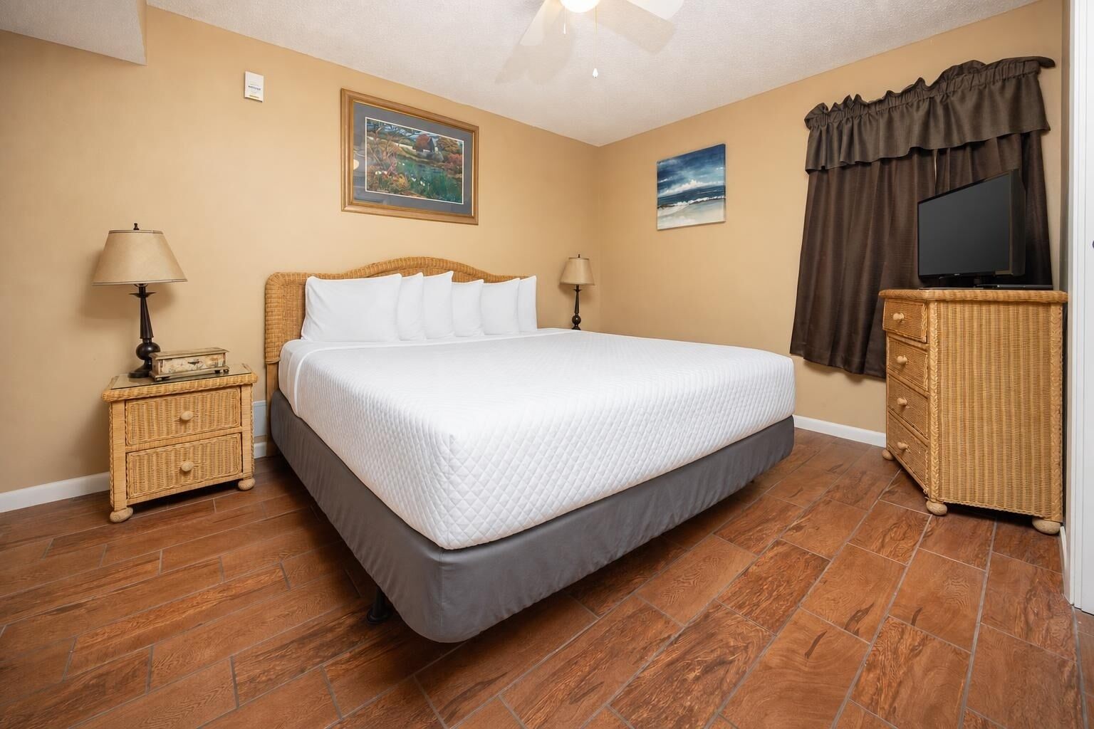 A bedroom with a bed, two nightstands, a dresser, a ceiling fan, and two wall-mounted paintings.