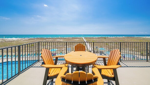 Un balcon avec une table et des chaises donnant sur une plage et une piscine.